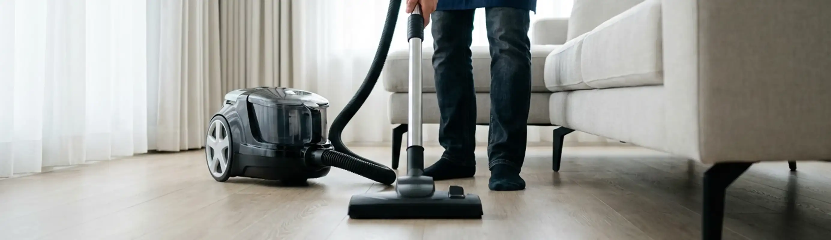 Professional house cleaner vacuuming a living room floor with a canister vacuum cleaner, Irvine, CA.
