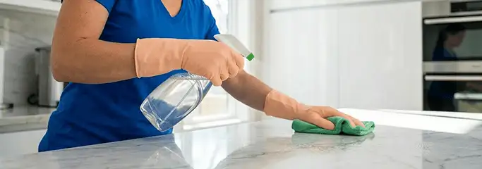 Maid service worker spraying and wiping a kitchen countertop with a microfiber cloth for sanitizing, Irvine, CA.