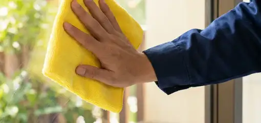 House cleaner wiping a glass window with a yellow microfiber cloth for streak-free cleaning, Irvine, CA.